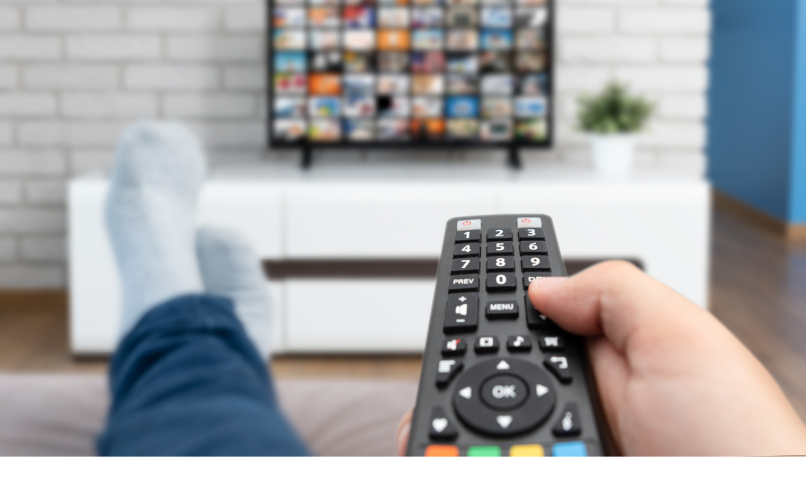 Person with their feet up points a remote at a TV.