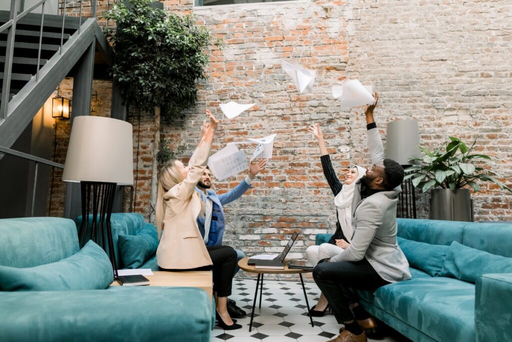 Celebration of success and great teamwork. Happy four multiethnic business people, men and women, throwing up work papers celebrating success and victory in joint financial project